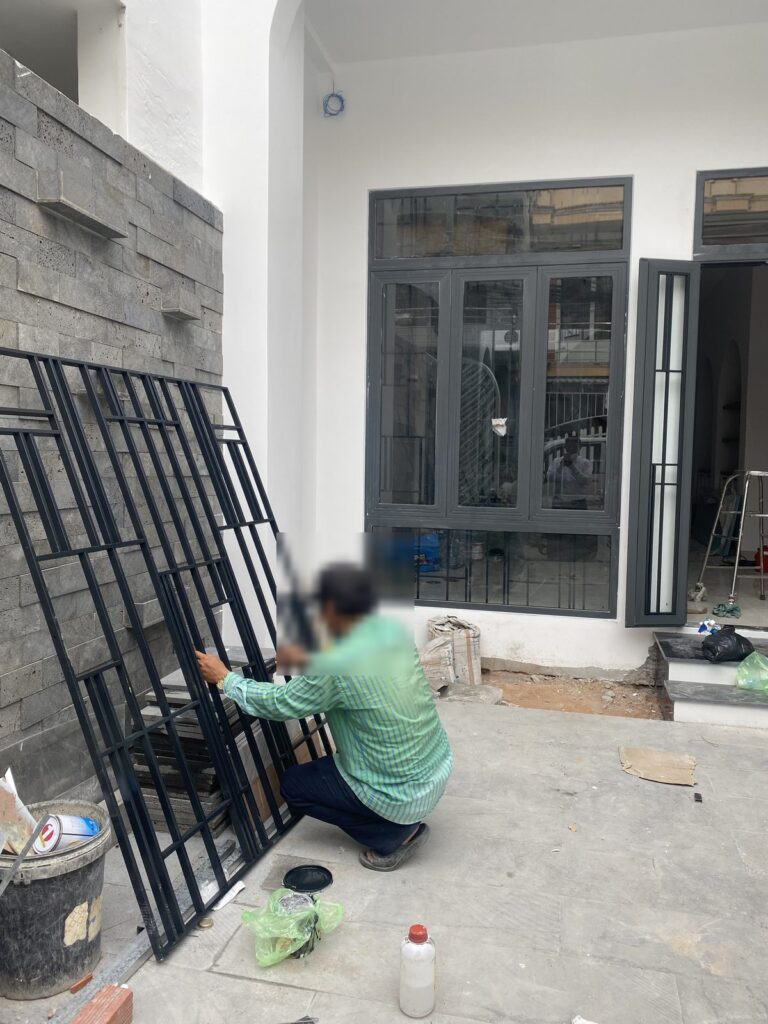 Thợ lắp khung cửa sắt sơn tĩnh điện trước cửa nhôm kính