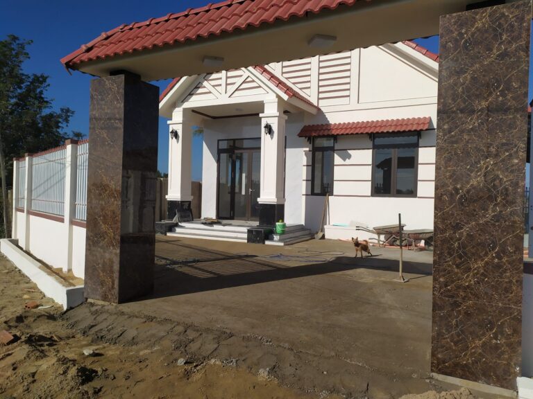 Nhà cấp 4 mái ngói đỏ nhìn từ cổng ốp đá, sân trước còn đang hoàn thiện